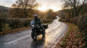 Motorcyclist riding along a wet, leaf-strewn British country road at low autumn sun